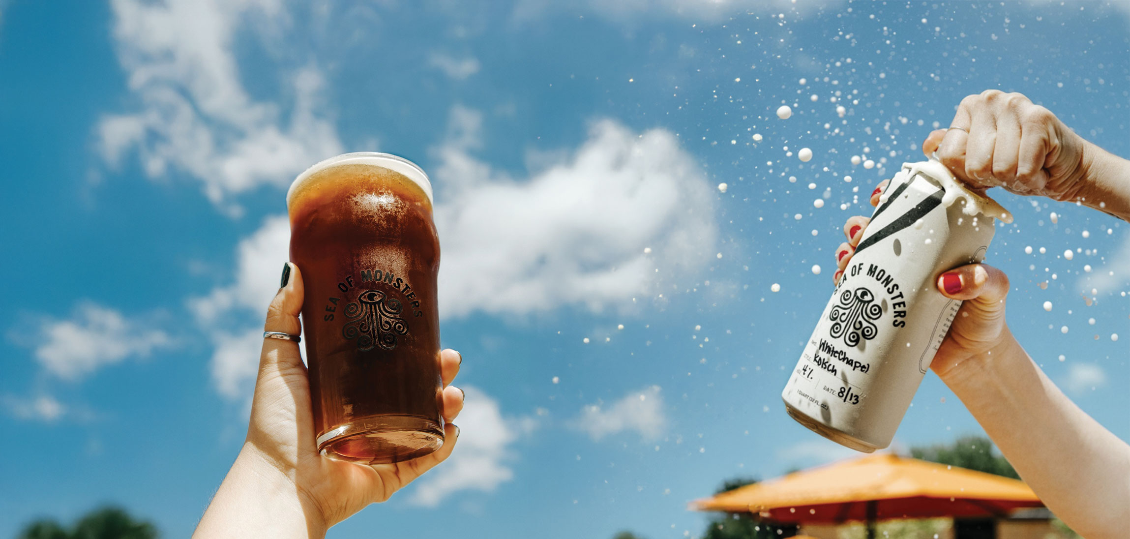 Sea of Monsters branded drinks held up outdoors, with a splashing can and bright blue sky in the background.